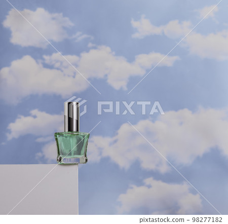 Transparent green perfume on white podium against cloudy blue sky. Concept of lightness of cosmetics Transparent green perfume on white podium against cloudy blue sky. Concept of lightness of cosmetics 98277182