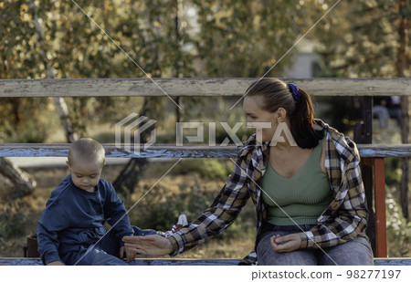 A little boy climbed up on the bench to his mother A little boy climbed up on the bench to his mother 98277197