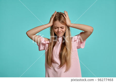 Studio portrait of a beautiful girl blonde teenager in a pink t-shirt posing over a blue background. 98277468
