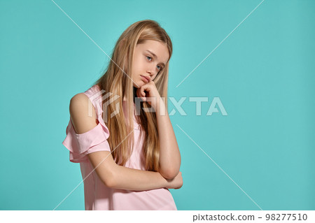 Studio portrait of a beautiful girl blonde teenager in a pink t-shirt posing over a blue background. Studio portrait of a beautiful girl blonde teenager in a pink t-shirt posing over a blue background. 98277510