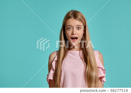 Studio portrait of a beautiful girl blonde teenager in a pink t-shirt posing over a blue background. Studio portrait of a beautiful girl blonde teenager in a pink t-shirt posing over a blue background. 98277519