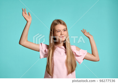Studio portrait of a beautiful girl blonde teenager in a pink t-shirt posing over a blue background. 98277536