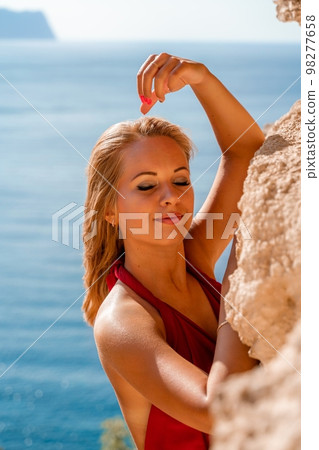 Smiling young woman in a red dress looks at the camera. A beautiful tanned girl enjoys her summer holidays at the sea. Portrait of a stylish carefree woman laughing at the ocean. Smiling young woman in a red dress looks at the camera. A beautiful tanned girl enjoys her summer holidays at the sea. Portrait of a stylish carefree woman laughing at the ocean. 98277658