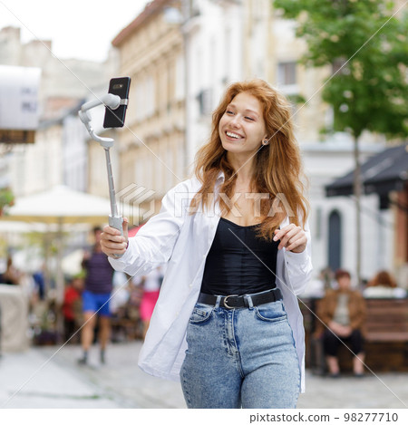 Young redheaded beautiful woman walking and using her mobile phone Young redheaded beautiful woman walking and using her mobile phone 98277710