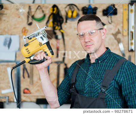 Portrait of a man with an electric jigsaw on wood in the workshop. 98278671