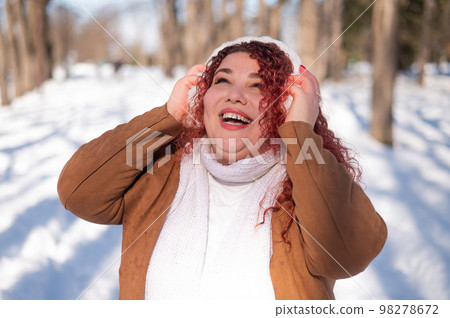 Cheerful fat caucasian woman in fur headphones outdoors. Cheerful fat caucasian woman in fur headphones outdoors. 98278672