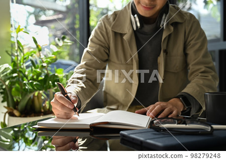 cropped shot of hipster man writing records to daily planner, working in bright modern home office cropped shot of hipster man writing records to daily planner, working in bright modern home office 98279248