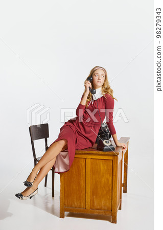 Stylish young woman, employee, personal assistant sitting on table and talking on phone over grey background 98279343