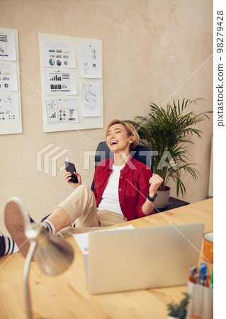 Business Woman Celebrate At Office. Cheerful Woman Holding Mobile And Feeling Happy Business Woman Celebrate At Office. Cheerful Woman Holding Mobile And Feeling Happy 98279428
