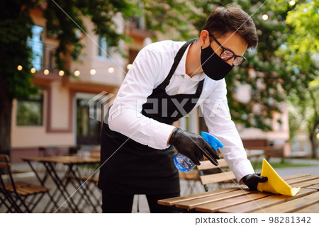Disinfecting to prevent COVID-19. Waiter in protective face mask and gloves cleaning. Disinfecting to prevent COVID-19. Waiter in protective face mask and gloves cleaning. 98281342