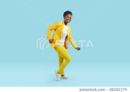 Happy beautiful African American woman in yellow suit dancing on blue background 98282174