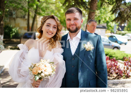 happy groom and bride in dress with open shoulders and a bouquet on the street. happy groom and bride in dress with open shoulders and a bouquet on the street. 98285891