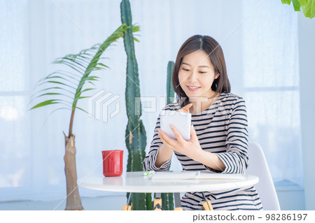 A woman holding a calculator and keeping a household account book in a bright living room A woman holding a calculator and keeping a household account book in a bright living room 98286197