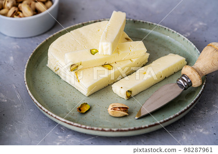 Italian cheese asiago with pistachios on stone black cutting board with cheese knife, pistachios in bowl and green napkin Italian cheese asiago with pistachios on stone black cutting board with cheese knife, pistachios in bowl and green napkin 98287961
