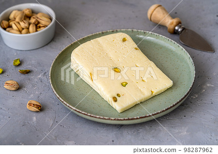 Italian cheese asiago with pistachios on stone black cutting board with cheese knife, pistachios in bowl and green napkin Italian cheese asiago with pistachios on stone black cutting board with cheese knife, pistachios in bowl and green napkin 98287962