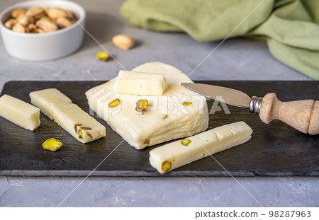 Italian cheese asiago with pistachios on stone black cutting board with cheese knife, pistachios in bowl and green napkin Italian cheese asiago with pistachios on stone black cutting board with cheese knife, pistachios in bowl and green napkin 98287963