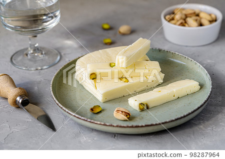 Italian cheese asiago with pistachios on stone black cutting board with cheese knife, pistachios in bowl and green napkin 98287964