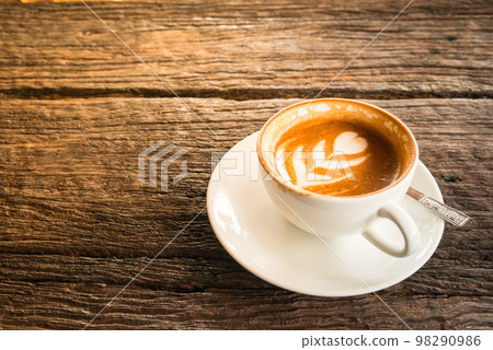 A cup of hot coffee with latte art on the surface placed in the wooden table. 98290986
