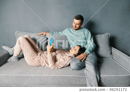 Smiling young couple embracing while looking at smartphone spending their time together at home Smiling young couple embracing while looking at smartphone spending their time together at home 98291172