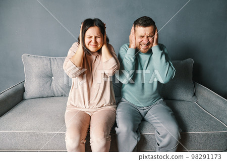 Stressed desperate couple closing ears with both hands irritated with loud annoying noise, having headache or migraine Stressed desperate couple closing ears with both hands irritated with loud annoying noise, having headache or migraine 98291173