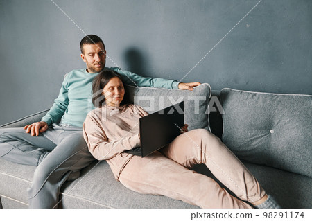 Happy couple embracing using laptop together relaxing on sofa Happy couple embracing using laptop together relaxing on sofa 98291174