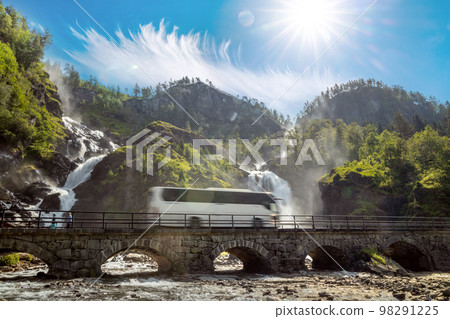 Tourist bus traveling on the road Latefossen Waterfall Odda Norway. Latefoss is a powerful, twin waterfall. Tourist bus traveling on the road Latefossen Waterfall Odda Norway. Latefoss is a powerful, twin waterfall. 98291225