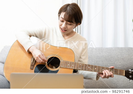 Smiling woman sitting on sofa playing guitar Smiling woman sitting on sofa playing guitar 98291746