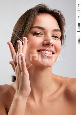 Close up beauty portrait of happy beautiful woman with bared shoulders applying face cosmetics products and looking with delighted facial expression isolated over light background Close up beauty portrait of happy beautiful woman with bared shoulders applying face cosmetics products and looking with delighted facial expression isolated over light background 98291876