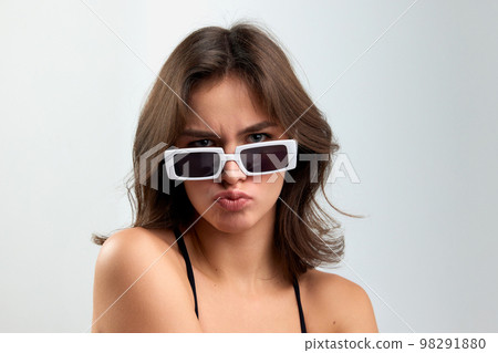 Doubts. Portrait of young stylish beautiful girl in fashionable eyewear isolated over grey background. Concept of beauty, skin care, cosmetology, fashion, makeup Doubts. Portrait of young stylish beautiful girl in fashionable eyewear isolated over grey background. Concept of beauty, skin care, cosmetology, fashion, makeup 98291880