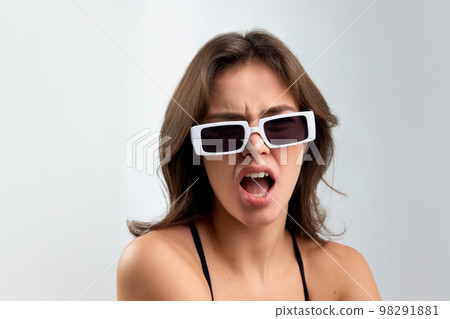 Young annoyed stylish beautiful girl in fashionable eyewear looking ahd shouting at camera isolated over grey background. Concept of beauty, fashion, facial expressions 98291881