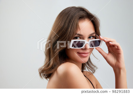 Portrait of young stylish beautiful girl in fashionable eyewear isolated over grey background. Concept of beauty, skin care, cosmetology, fashion, makeup Portrait of young stylish beautiful girl in fashionable eyewear isolated over grey background. Concept of beauty, skin care, cosmetology, fashion, makeup 98291883