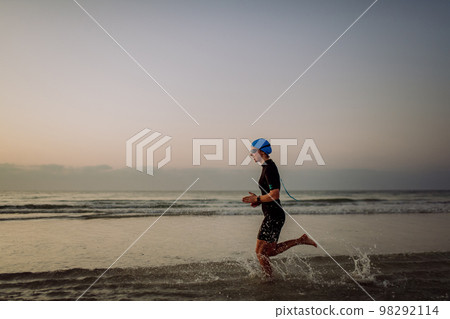 Side view of young woman in neoprene running in the ocean. 98292114
