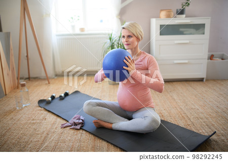 Pregnant woman doing exercises with ball in her apartment. Pregnant woman doing exercises with ball in her apartment. 98292245