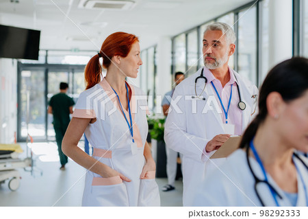 Older doctor giving advise to his younger colleague, discussing at hospital corridor. Health care concept. Older doctor giving advise to his younger colleague, discussing at hospital corridor. Health care concept. 98292333