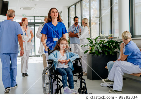 Young nurse pushing little girl on wheelchair at hospital corridor. Young nurse pushing little girl on wheelchair at hospital corridor. 98292334