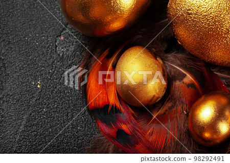 Golden Easter eggs on red bird feathers close up Golden Easter eggs on red bird feathers close up 98292491