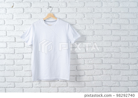 White t-shirt hanging on hanger against brick wall 98292740