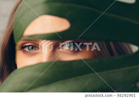 Attractive young woman hiding behind monstera leaf 98292901