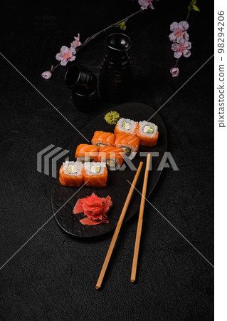 salmon sushi roll with red caviar, chopsticks, bottle of sake and cups on black salmon sushi roll with red caviar, chopsticks, bottle of sake and cups on black 98294206