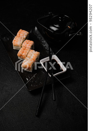 Shrimp sushi roll, soy sauce, chopsticks and black teapot on black Shrimp sushi roll, soy sauce, chopsticks and black teapot on black 98294207