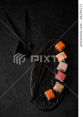 Different kind of sushi roll, soy sauce and chopsticks on black concrete background Different kind of sushi roll, soy sauce and chopsticks on black concrete background 98294215