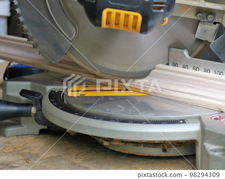 miter saw in the process of sawing a wooden plank close-up, sawing a wooden material on a miter cut, carpentry machinery in the process of work 98294309