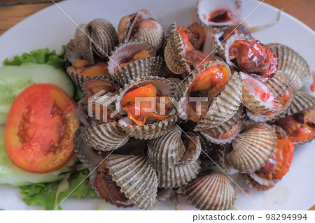 Steamed cockles (boiled cockles) are placed on a white plate. Garnished with sliced tomatoes. 98294994