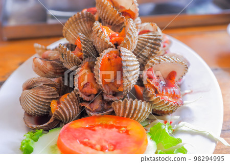 Steamed cockles (boiled cockles) are placed on a white plate. Garnished with sliced tomatoes. 98294995