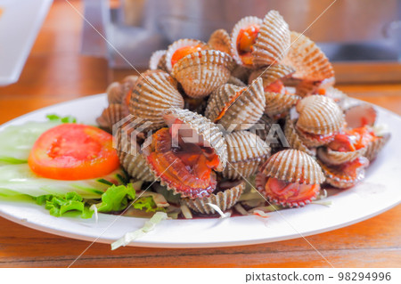 Steamed cockles (boiled cockles) are placed on a white plate. Garnished with sliced tomatoes. 98294996