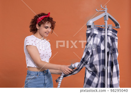 A woman with a smile on her face irons a man's shirt with a steamer. A woman with a smile on her face irons a man's shirt with a steamer. 98295040