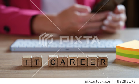 IT specialist working on keyboard at office desk, wooden cubes with words IT career in front of him. 98295175