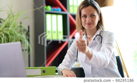 Female doctor sitting at her desk in medical clinic and shows thumb up. Female doctor sitting at her desk in medical clinic and shows thumb up. 98295186