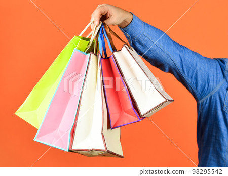 Hand hold bags. Shopping bags in hand on red background. Paper bags different colors. Shopping in mall. Black friday concept. Holidays preparation and celebration. Gift and present. Delivery 98295542