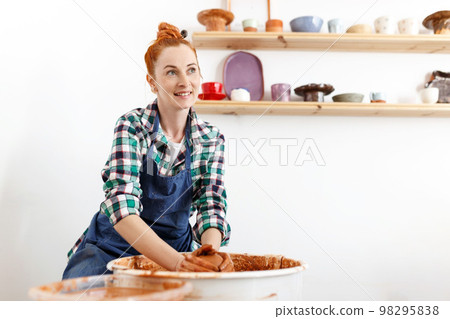 Cheerful female sculptor while she making clay pot on pottery wheel. Idea of small business and entrepreneurship. Home hobby, entertainment and leisure. Art studio 98295838